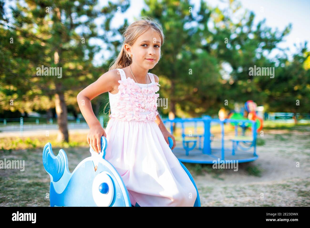 Una hermosa niña en un maravilloso rosa delicado vestido largo se sienta en  un pequeño columpio en un cálido parque soleado de verano en unas  vacaciones muy esperadas Fotografía de stock -