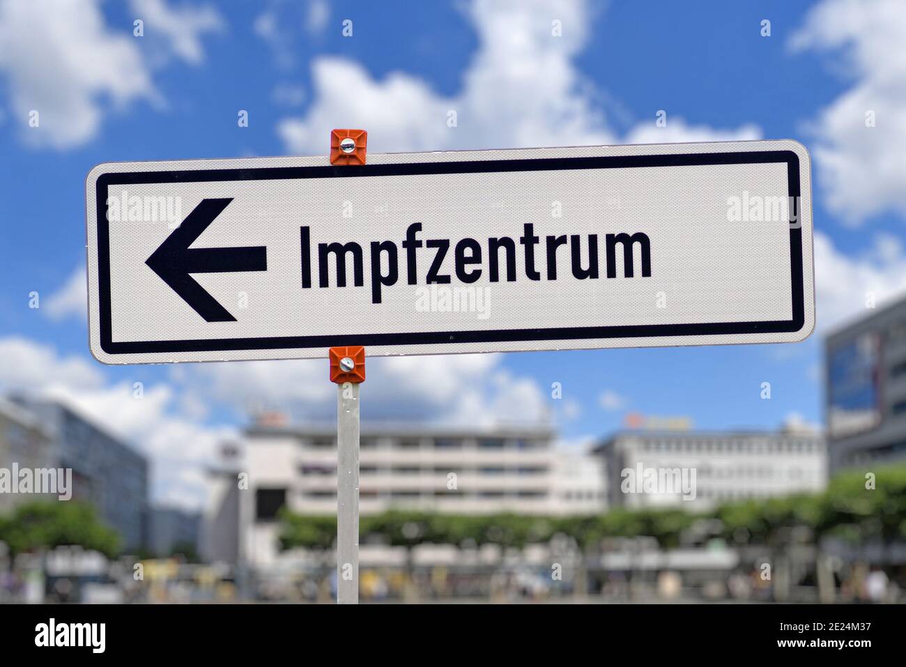 Señal blanca de la calle alemana que apunta hacia el centro de vacunación llamado 'Impfzentrum' Establecer para vacunar a las personas contra el virus de la Corona en fornt de cit borroso Foto de stock