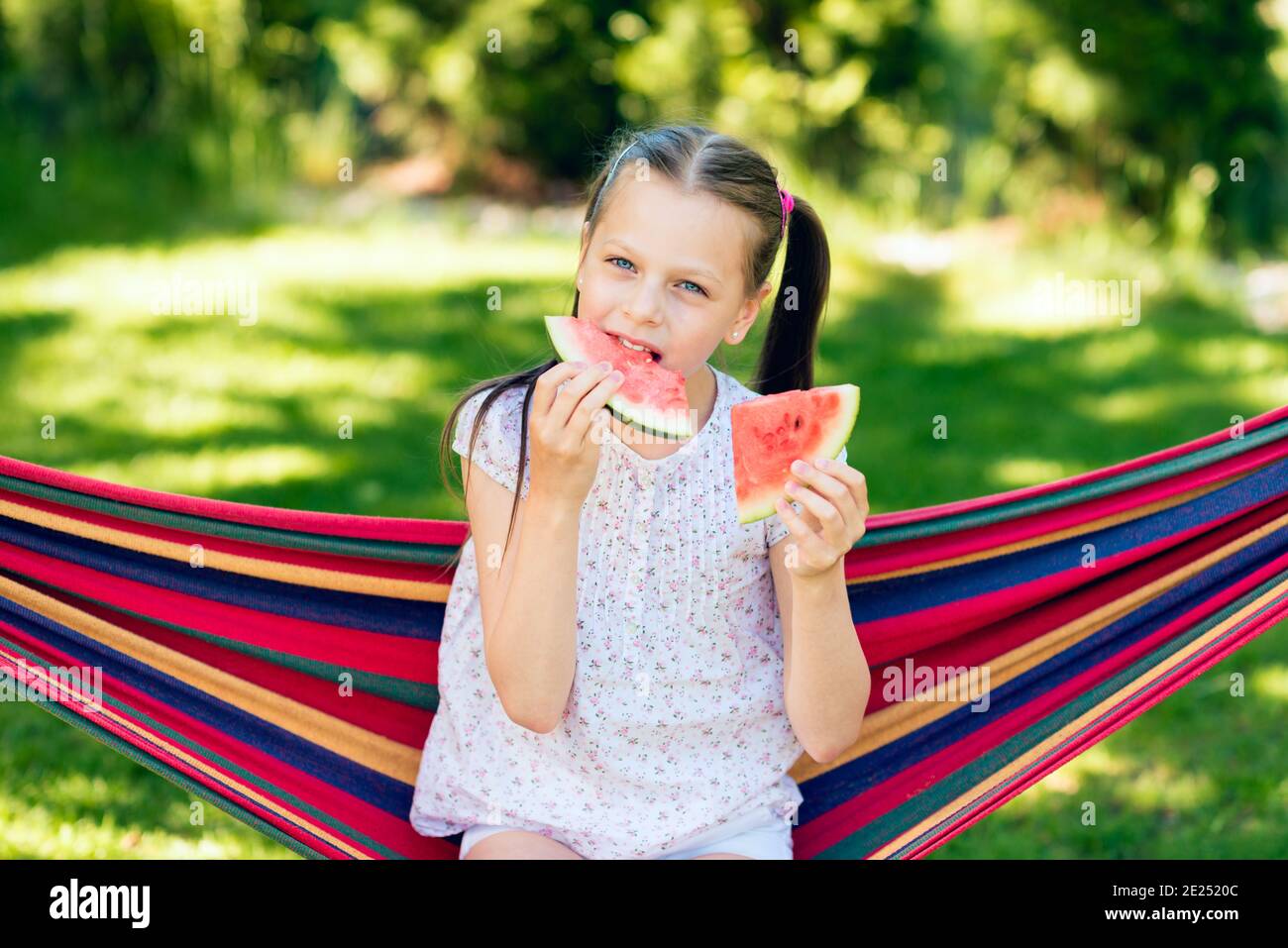 Niña comiendo rodajas de sandía en el jardín sentada una hamaca Fotografía  de stock - Alamy