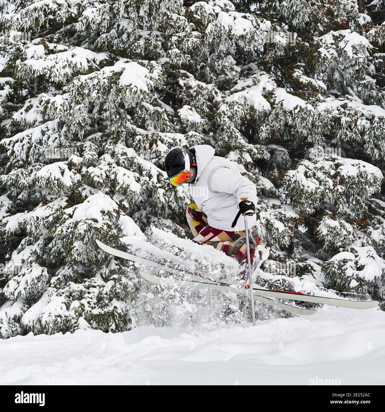 Esquiador masculino esquiando en nieve fresca en polvo con hermosos árboles nevados en el fondo. Hombre freerider en gafas de esquí haciendo saltar mientras se desliza por las pistas cubiertas de nieve. Concepto de deportes de invierno Foto de stock