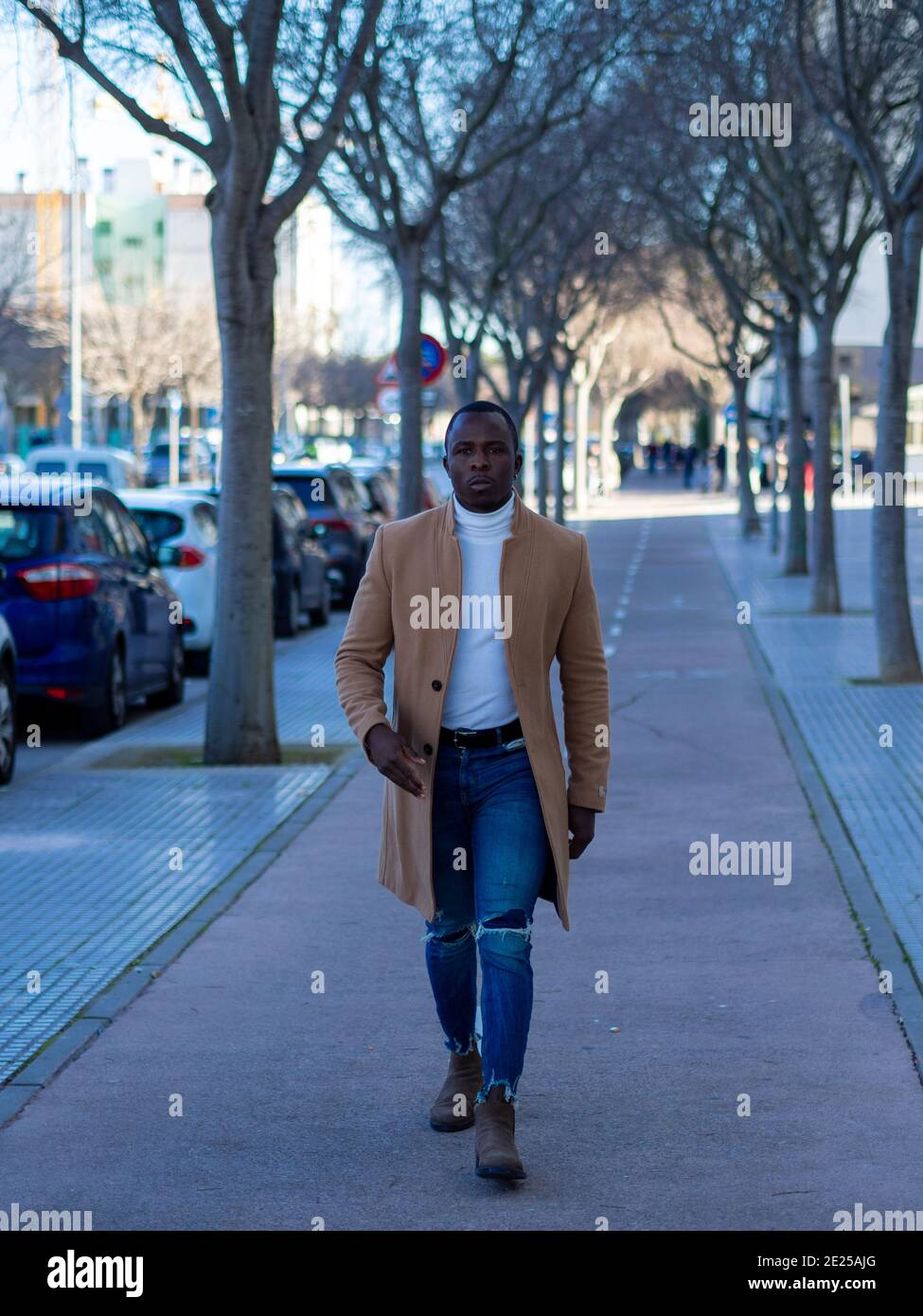 Hombre africano con estilo con jeans con un suéter blanco y.. bata de color  beige mientras camina por la calle Fotografía de stock - Alamy