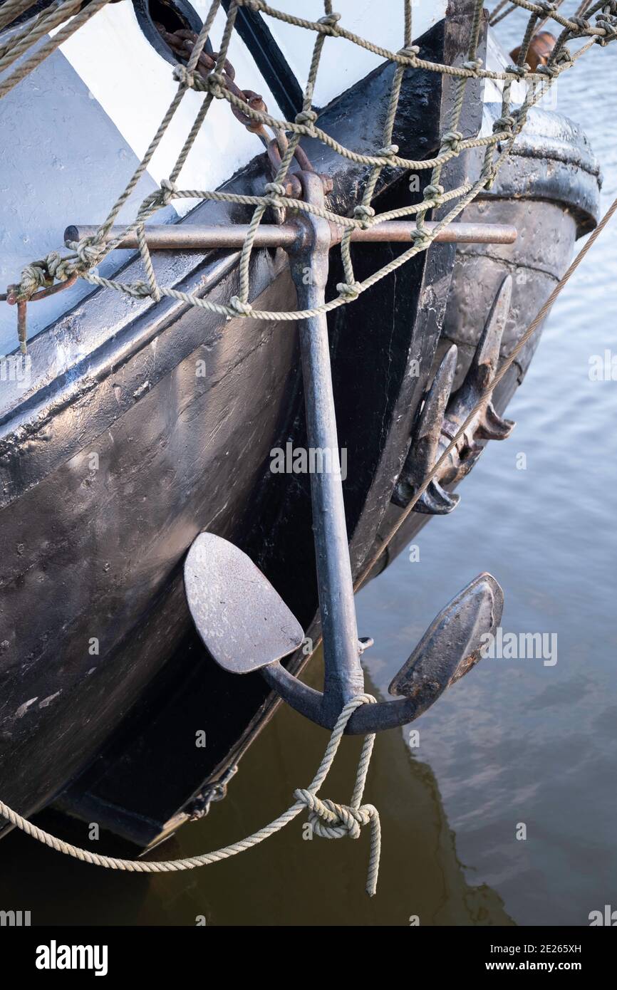 El ancla cuelga contra el arco de acero redondo de un viejo barco de pesca de acero Foto de stock
