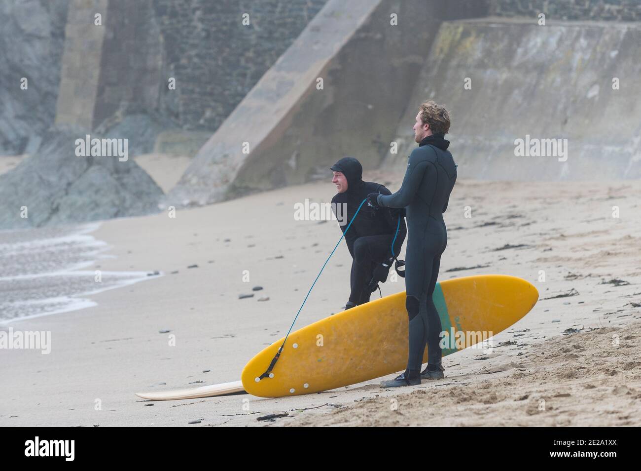 Surfistas que se preparan para comenzar una sesión de surf en las frías condiciones climáticas invernales en Great Western Beach en Newquay en Cornwall. Foto de stock