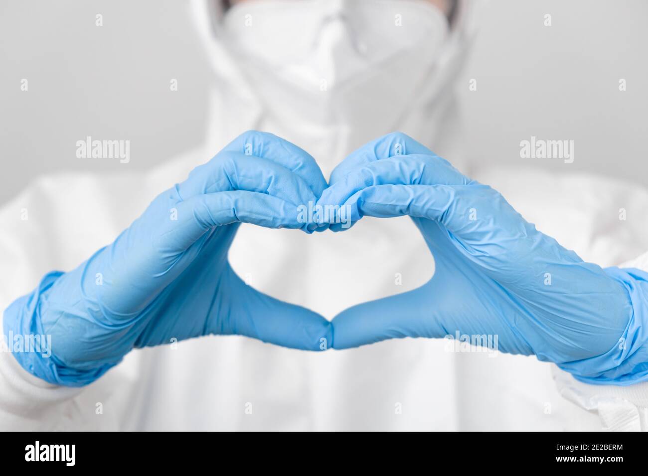 Doctor en un traje de protección de riesgo biológico PPE y máscara protectora frente al coronavirus, Sars-COV-2, Covid-19 sosteniendo las manos en forma de corazón en azul Foto de stock