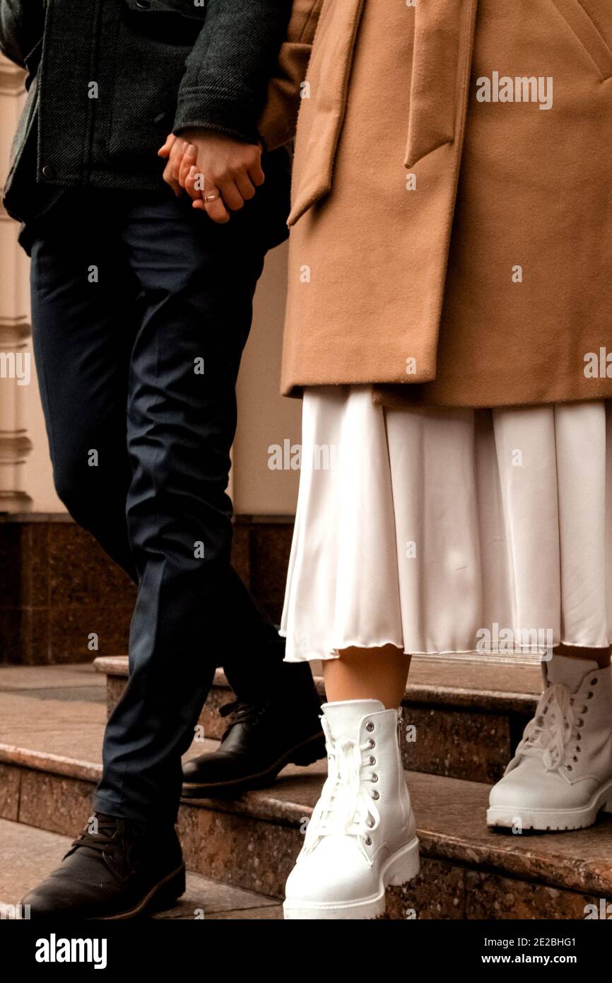 un chico y una chica van de la mano por la calle. chica en un vestido y  abrigo, un chico en un traje Fotografía de stock - Alamy