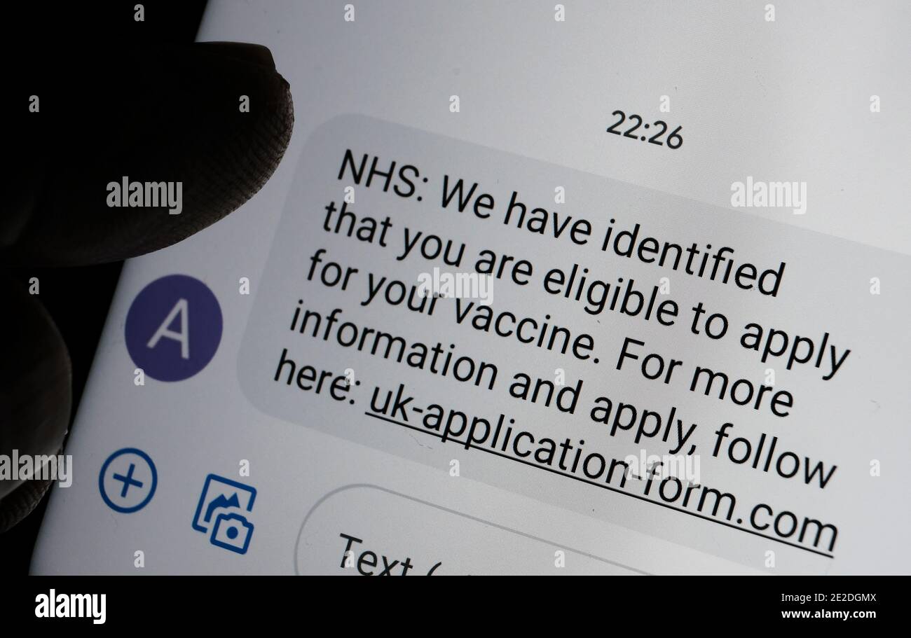 Stafford, Reino Unido - Enero 13 2021: Mensaje de texto de la vacuna contra el estafa coronavirus visto en la pantalla del smartphone y silueta borrosa de la punta del dedo Foto de stock