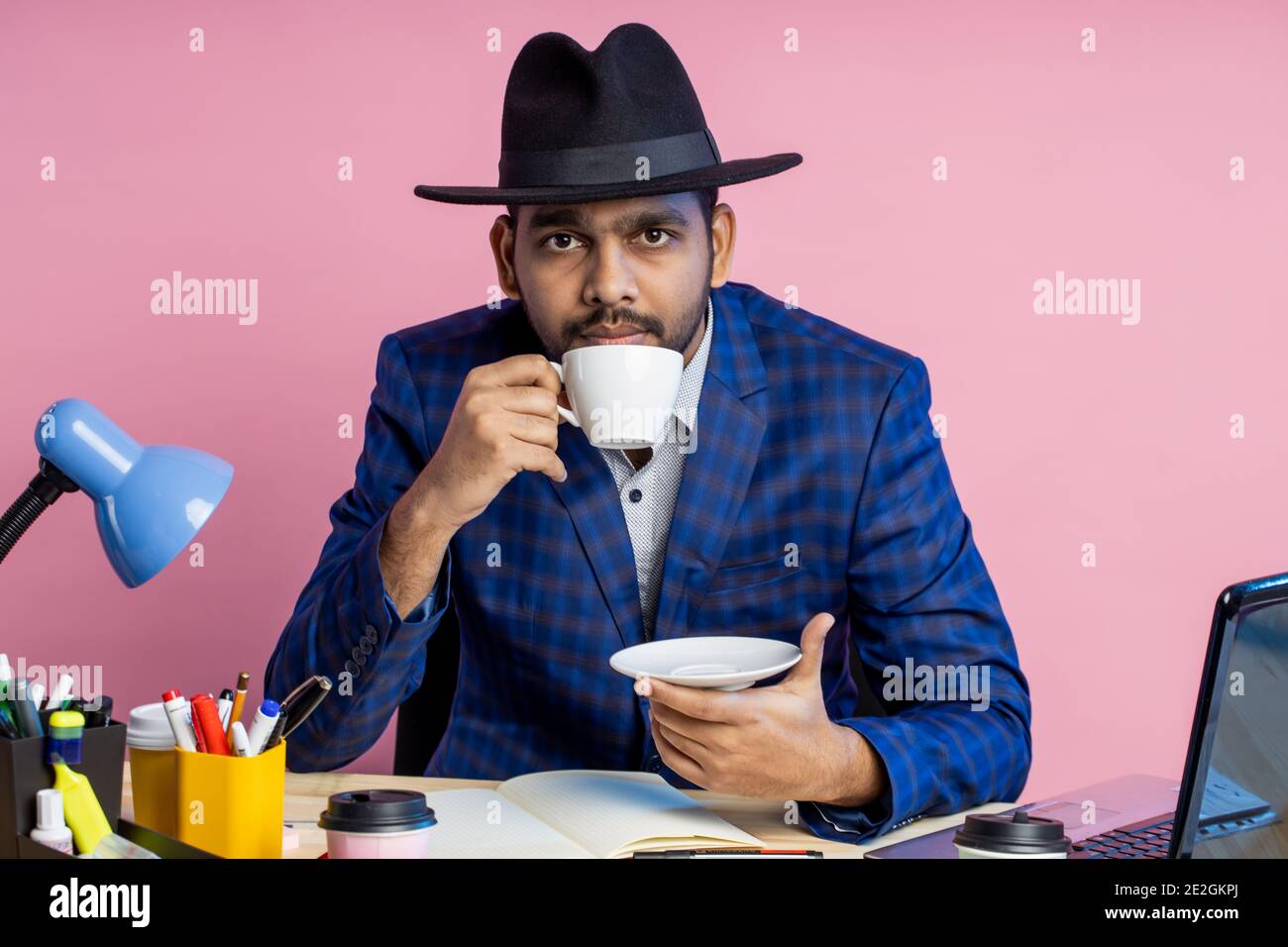 hombre de negocios con traje de cuadros formal, sombrero negro, sentado en  el lugar de trabajo, pensando en algo, mirando a un lado, disfrutando de un  café aromático. Negocios, l Fotografía de