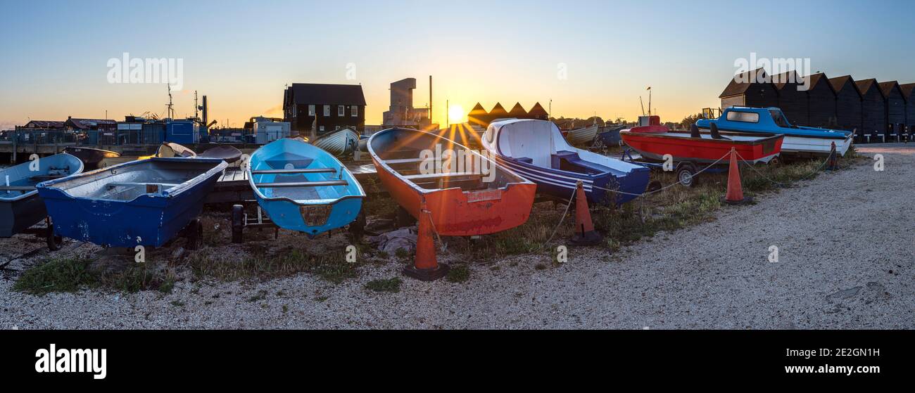 Filas de coloridos barcos en la costa norte de Kent en Whitstable con las icónicas cabañas de pescadores y obras en el fondo. Foto de stock