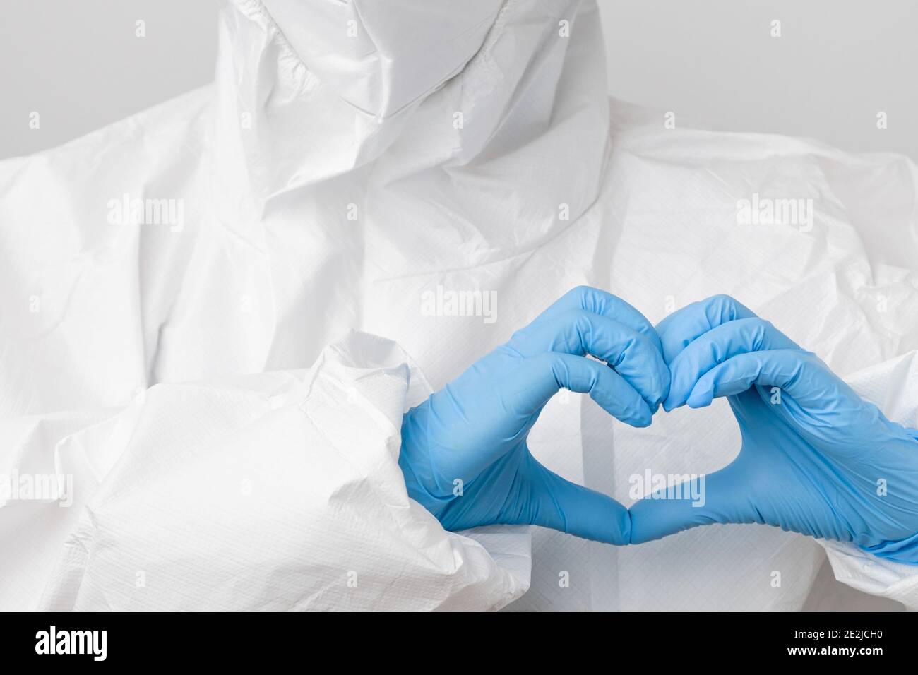 Doctor en un traje de protección de riesgo biológico PPE y máscara protectora frente al coronavirus, Sars-COV-2, Covid-19 sosteniendo las manos en forma de corazón en azul Foto de stock