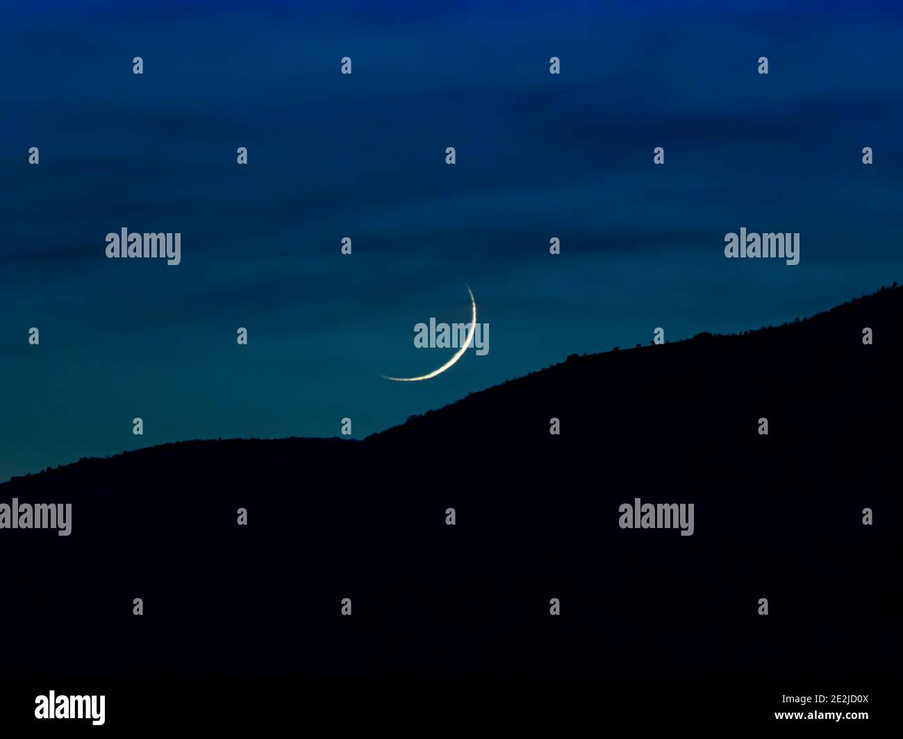 Centrado sólo arco Azul cielo Luna bajo en el horizonte sobre la silueta de la montaña Foto de stock