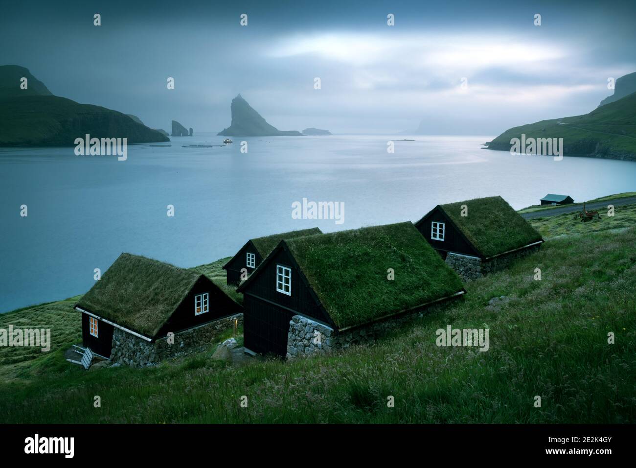 Vista pintoresca de las casas cubiertas de hierba faroesa tradicional en el pueblo de Buur. Drangarnir y Tindholmur se apilan sobre el fondo. Isla Vagar, Islas Feroe, Dinamarca. Fotografía de paisajes Foto de stock