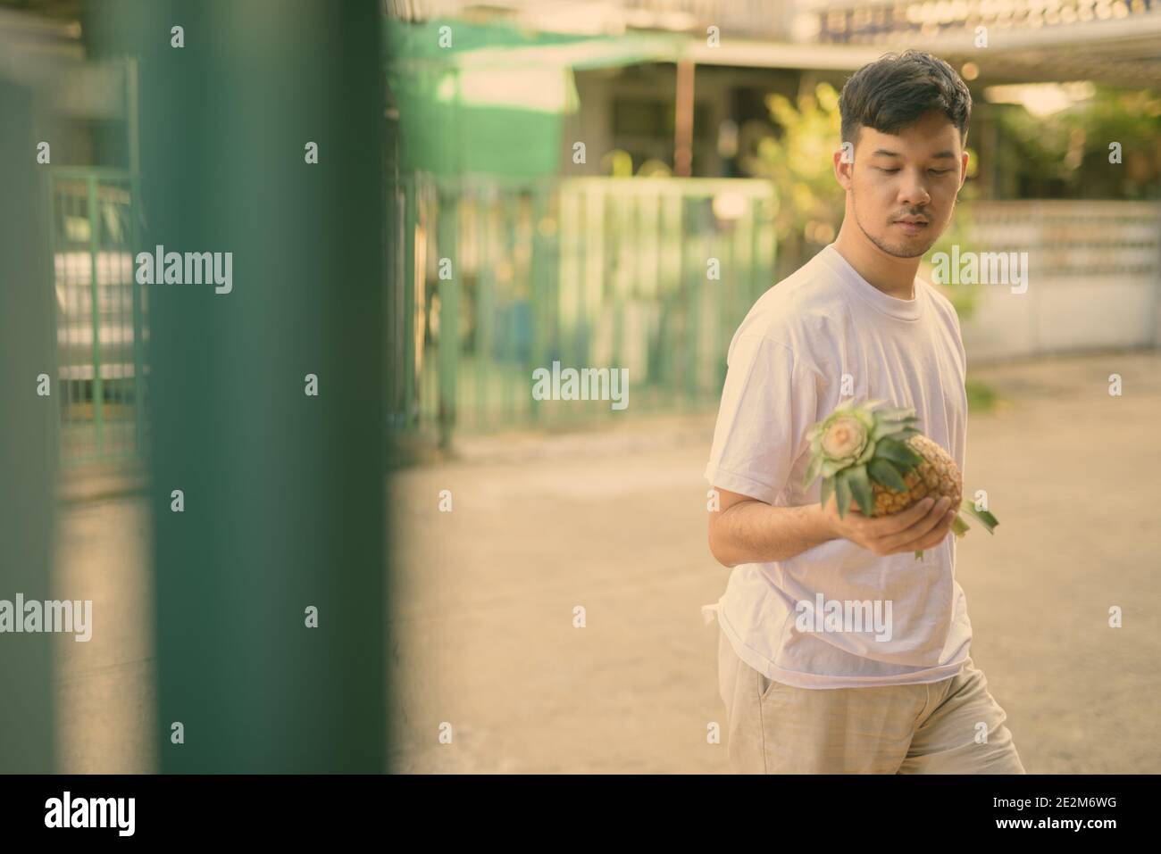 Joven hombre asiático trayendo la piña en casa Foto de stock