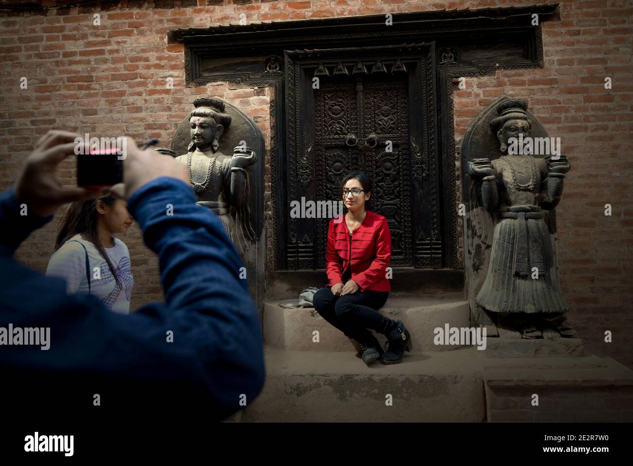 Un visitante posando para una foto frente a una puerta en el palacio de 'cincuenta y cinco ventanas' en Bhaktapur. Durbar Square, Bhaktapur, Bagmati, Nepal. Foto de stock