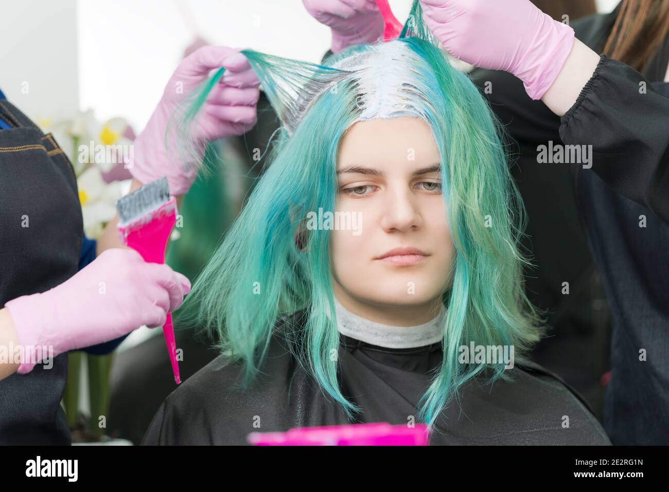 Dos peluqueros usan cepillo rosa al aplicar pintura al cabello durante el  proceso de blanquear las raíces del cabello. Lindo joven adulto caucásico  cliente con pelo largo Fotografía de stock - Alamy