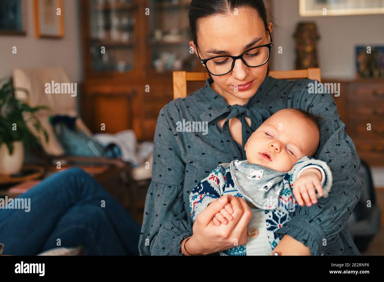 Madre joven sentada en la sala de estar y sosteniendo al bebé recién nacido Foto de stock