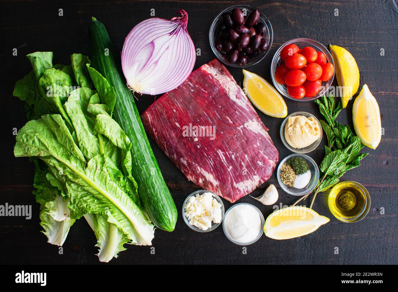 Mediterranean Steak Bowl Ingredientes: Filete de flanco crudo, frutas, verduras y hierbas utilizadas para hacer ensalada sobre un fondo de madera oscura Foto de stock