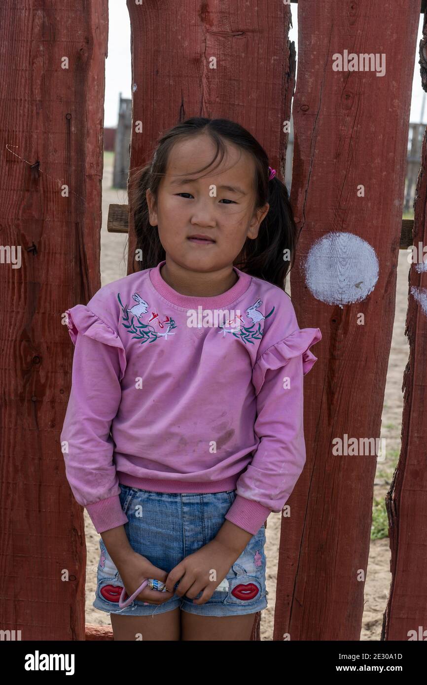 Olgii, Mongolia - 7 de agosto de 2019: Joven mongol con suéter púrpura frente a una valla roja. Foto de stock