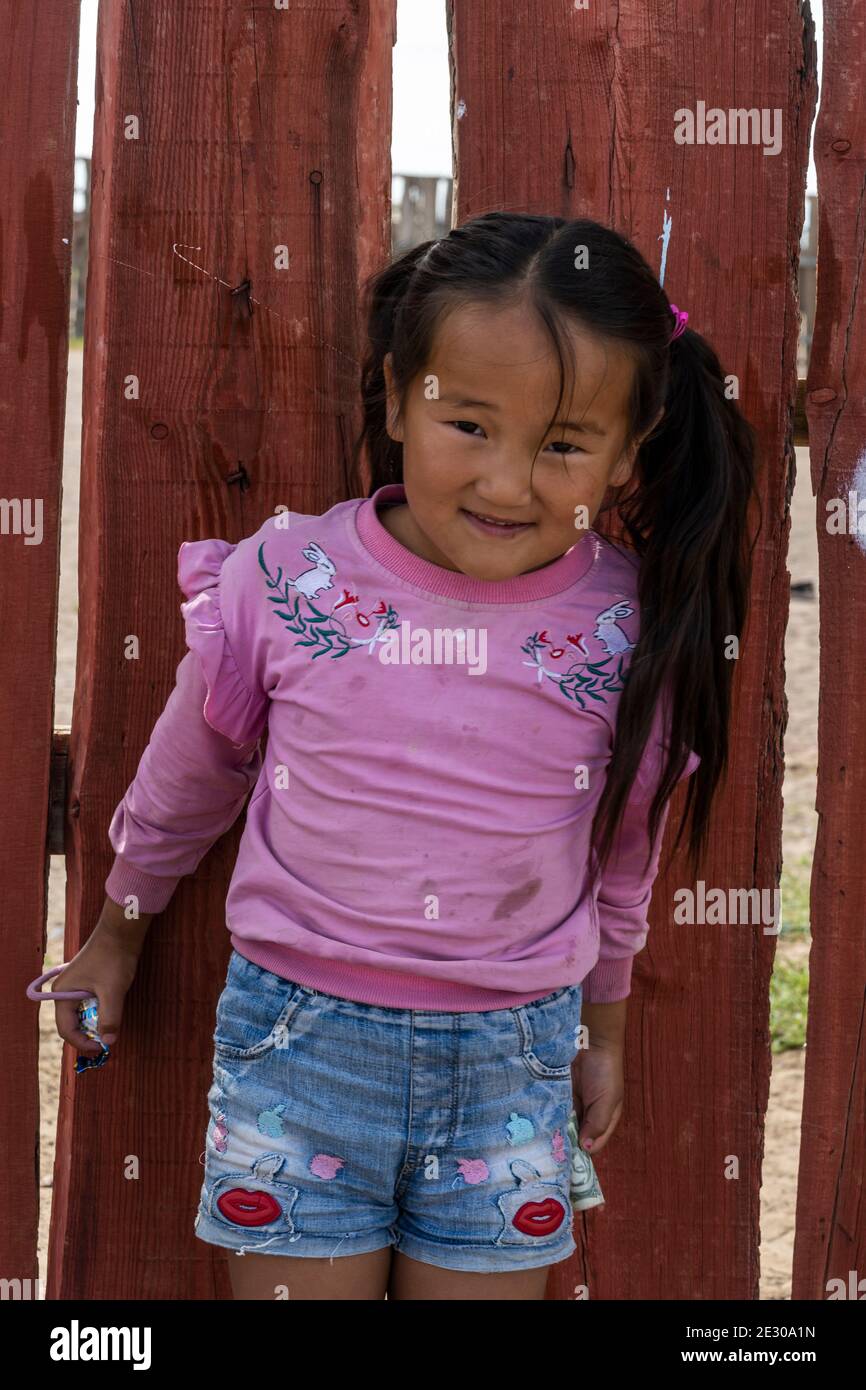 Olgii, Mongolia - 7 de agosto de 2019: Joven mongol sonriendo y con suéter púrpura frente a una valla roja. Foto de stock