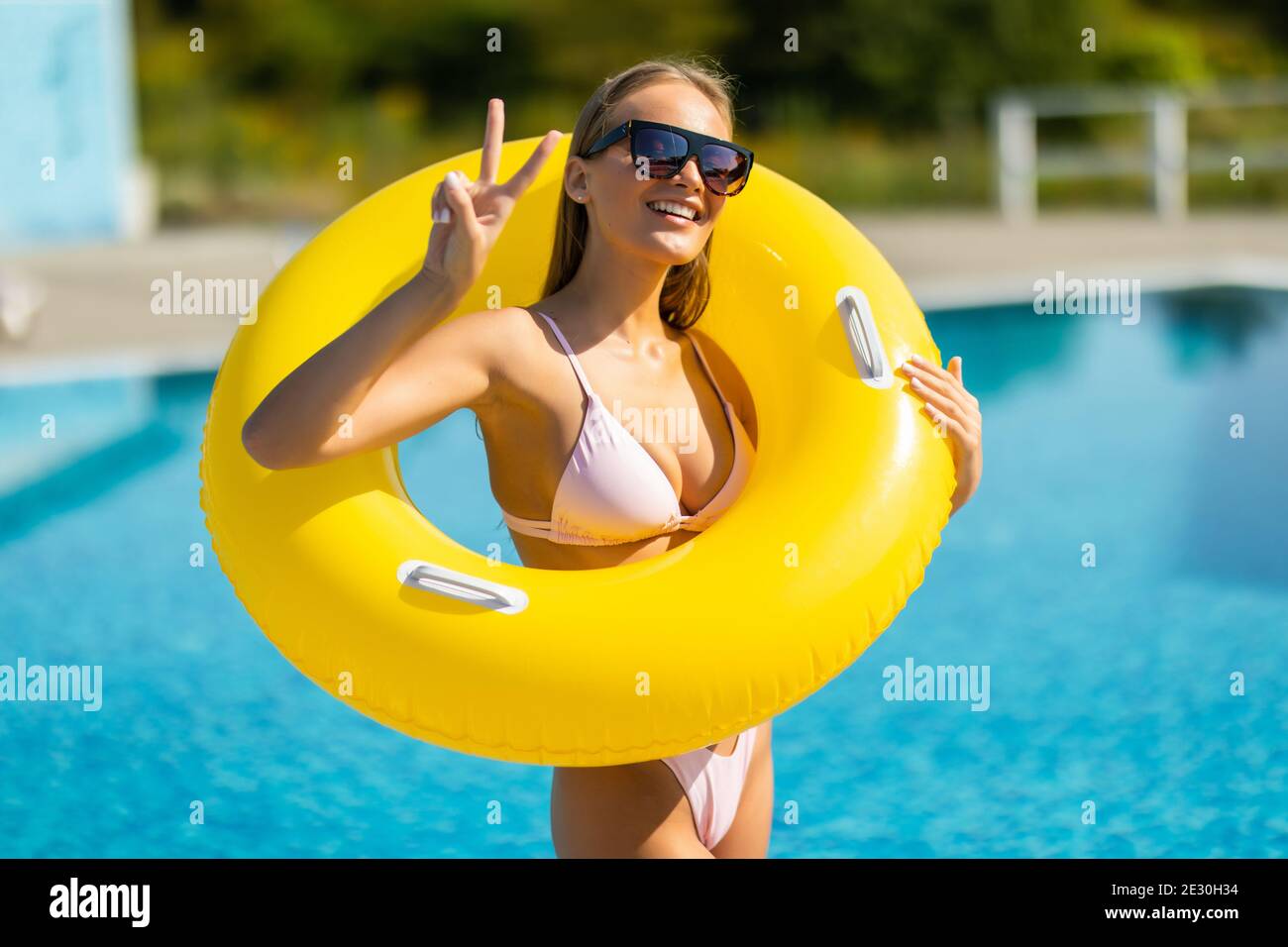 Bella mujer en bikini sosteniendo un anillo inflable en la piscina y  sonriente. Mujeres vistiendo bikini y gafas de sol disfrutando de sus  vacaciones en piscinas del complejo Fotografía de stock -