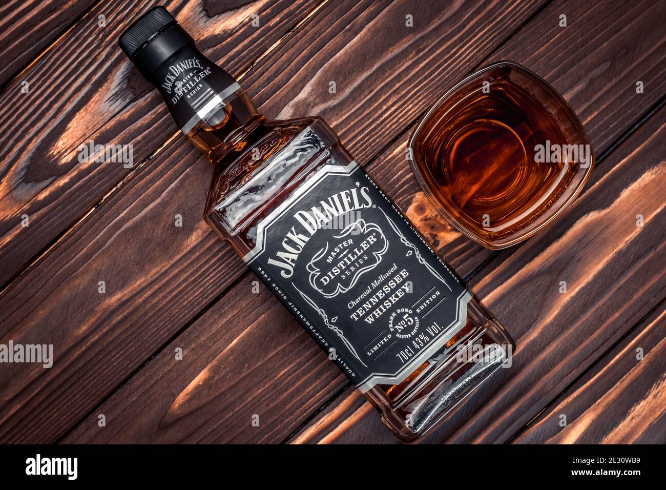 Kharkiv, Ucrania, 14 de enero de 2021: Botella llena del número 5 de Jack Daniel en tablas de madera marrón oscuro. Un vaso de whisky americano. Bebida fuerte. Antiguo br Foto de stock