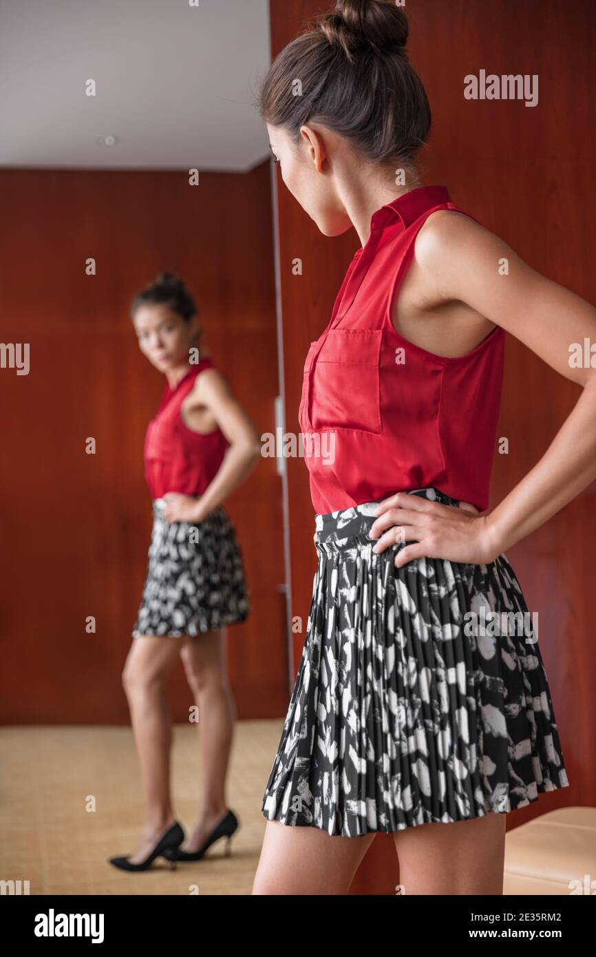 Mujer mirando en espejo feliz de pérdida de peso imagen corporal. Chica asiática que intenta en la ropa elegir qué traje a usar para el trabajo en casa. Forma y estilo Foto de stock