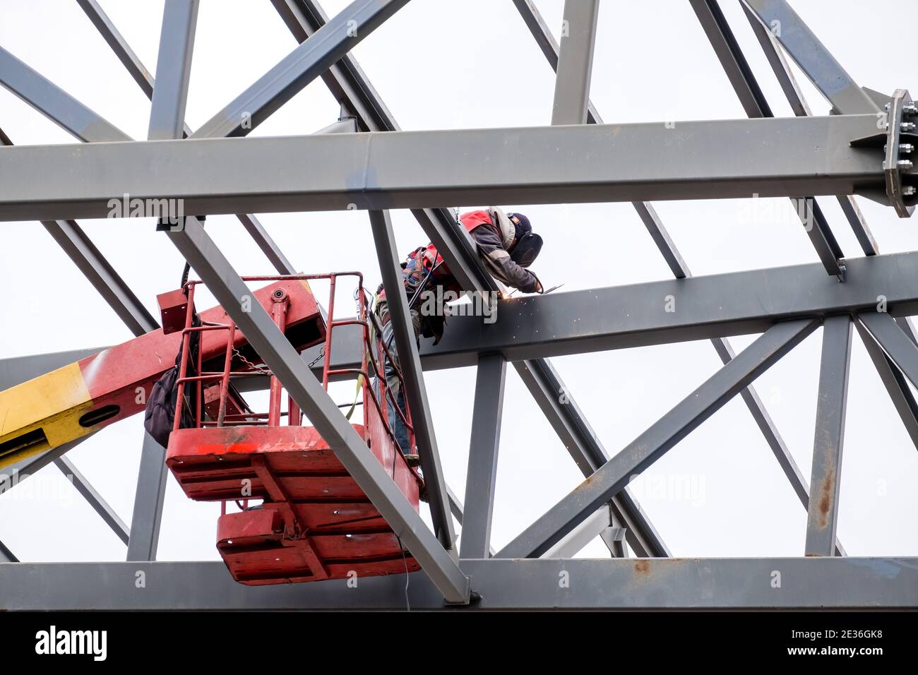 El hombre soldador que trabaja en una grúa realiza trabajos de gran altura  en la soldadura de estructuras metálicas de una nueva torre a una altura.  Aislado sobre fondo blanco Fotografía de