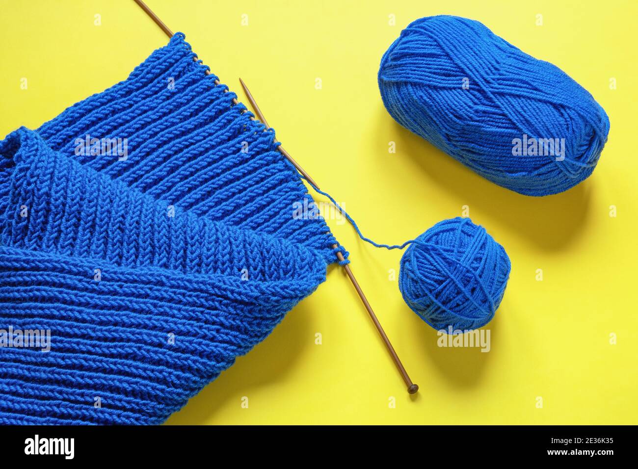 Tejer. Bufanda azul brillante con agujas de punto y bola de lana sobre  fondo amarillo Fotografía de stock - Alamy