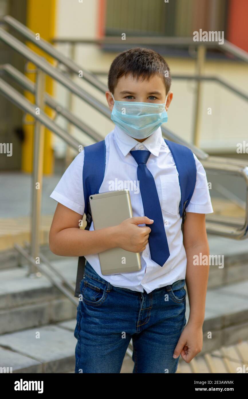 un niño en una camisa blanca, corbata azul y una mochila se coloca en una  máscara médica con una tableta Fotografía de stock - Alamy