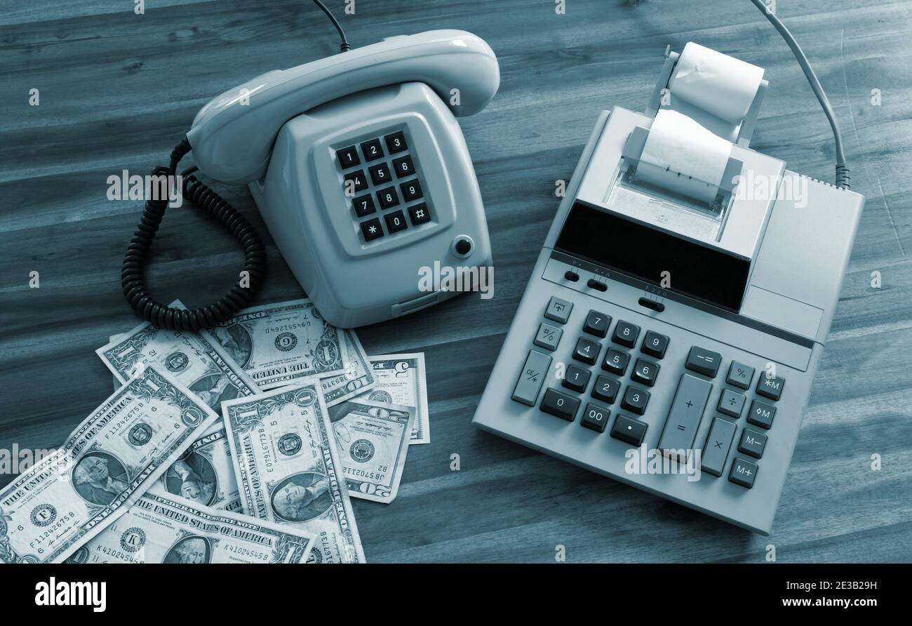 Calculadora antigua, teléfono y dólares en el escritorio Foto de stock