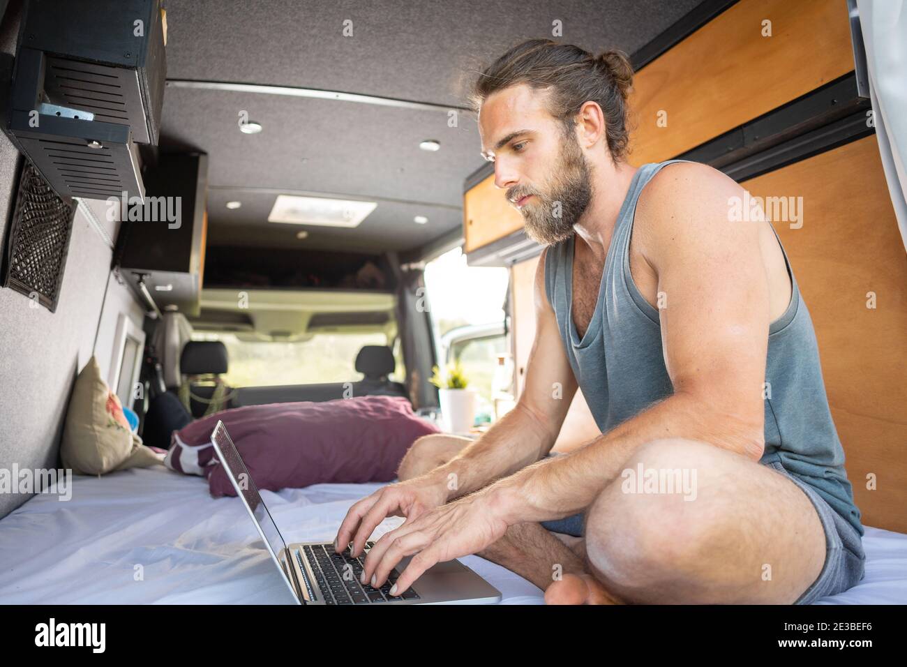 Hombre sentado dentro de una furgoneta de autocaravana usando un ordenador portátil Foto de stock