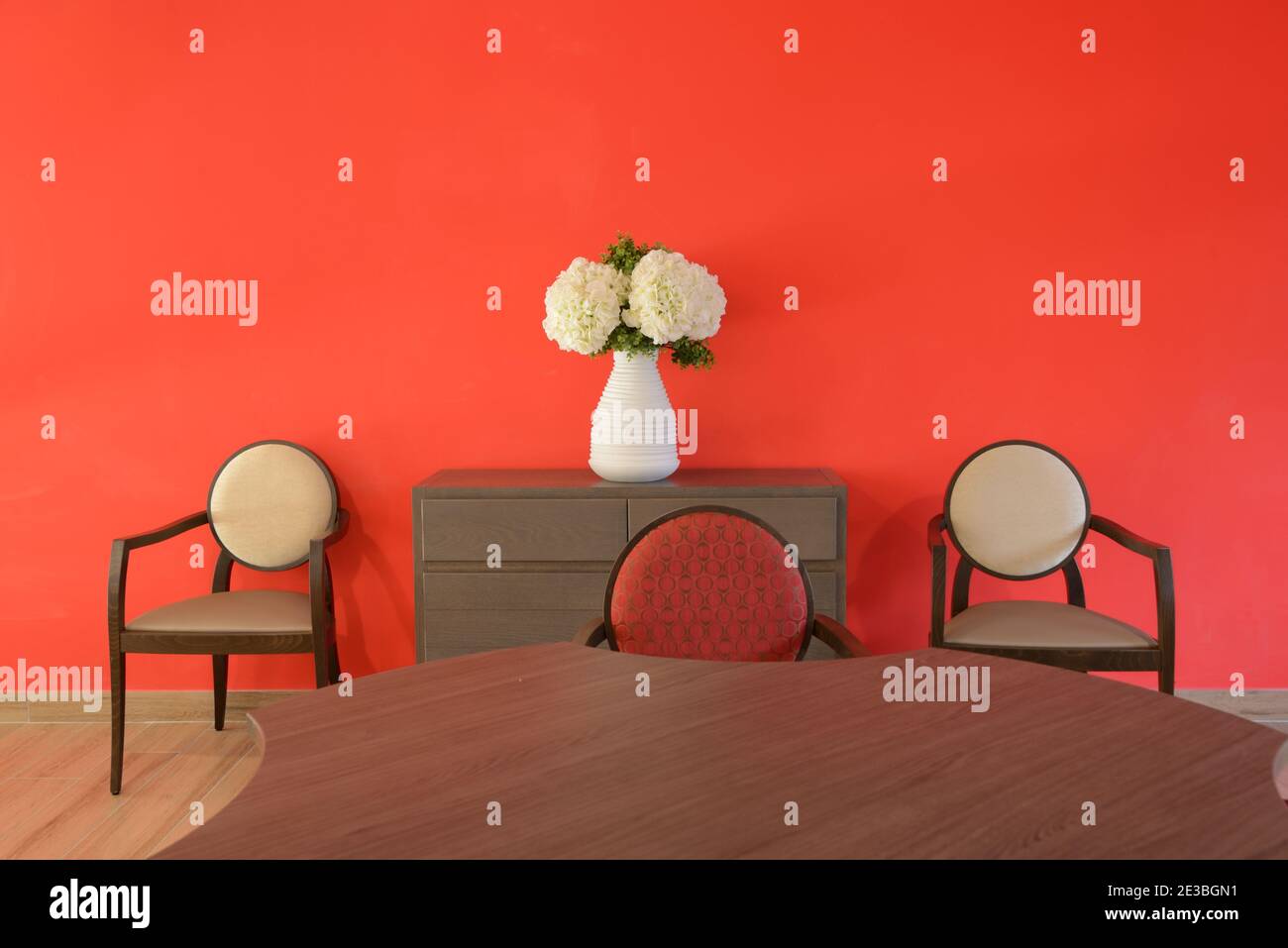 Comedor minimalista contemporáneo con mesa de comedor y comedor moderno Sillas fotografiadas contra una pared roja Foto de stock