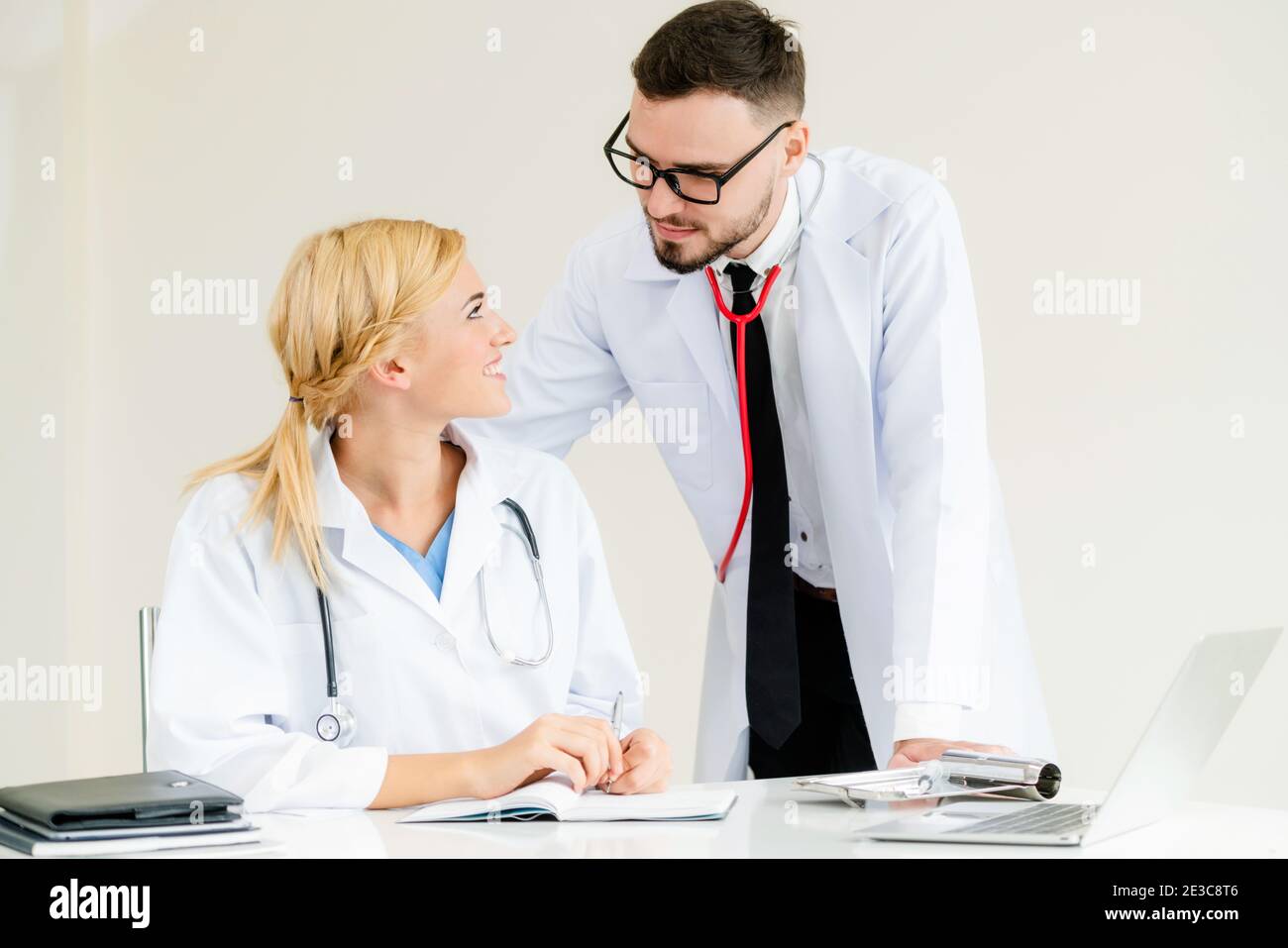 Doctor en el hospital office escribe notas sobre los pacientes informan al tener una conversación con otro médico que de pie junto a ella. Foto de stock