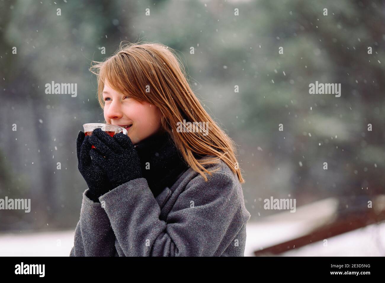 Desde el frío, una niña congelada sostiene una taza de té caliente,  disfruta del aroma y mira al lado contra el fondo de un bosque de invierno  Fotografía de stock - Alamy