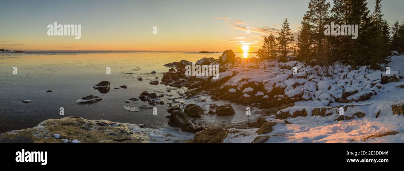Vista panorámica de la puesta de sol de invierno escénica sobre el mar, grandes piedras en la costa y el bosque de la península de Kont, Umea, Suecia. Invierno pinos escandinavos. Foto de stock