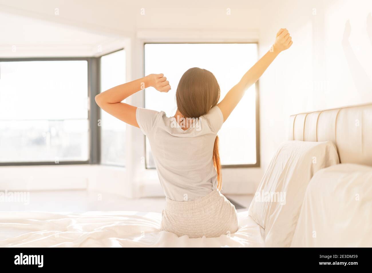 La mujer de la mañana se despierta en la cama al amanecer y la luz del sol  brilla desde la ventana. Niña feliz de pájaro temprano en pijamas el fin de  semana