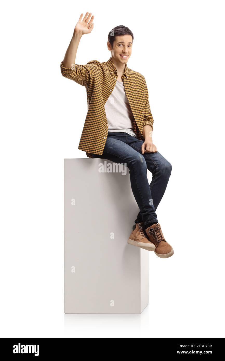 Tímido joven sentado en una columna blanca y agitando aislado sobre fondo blanco Foto de stock