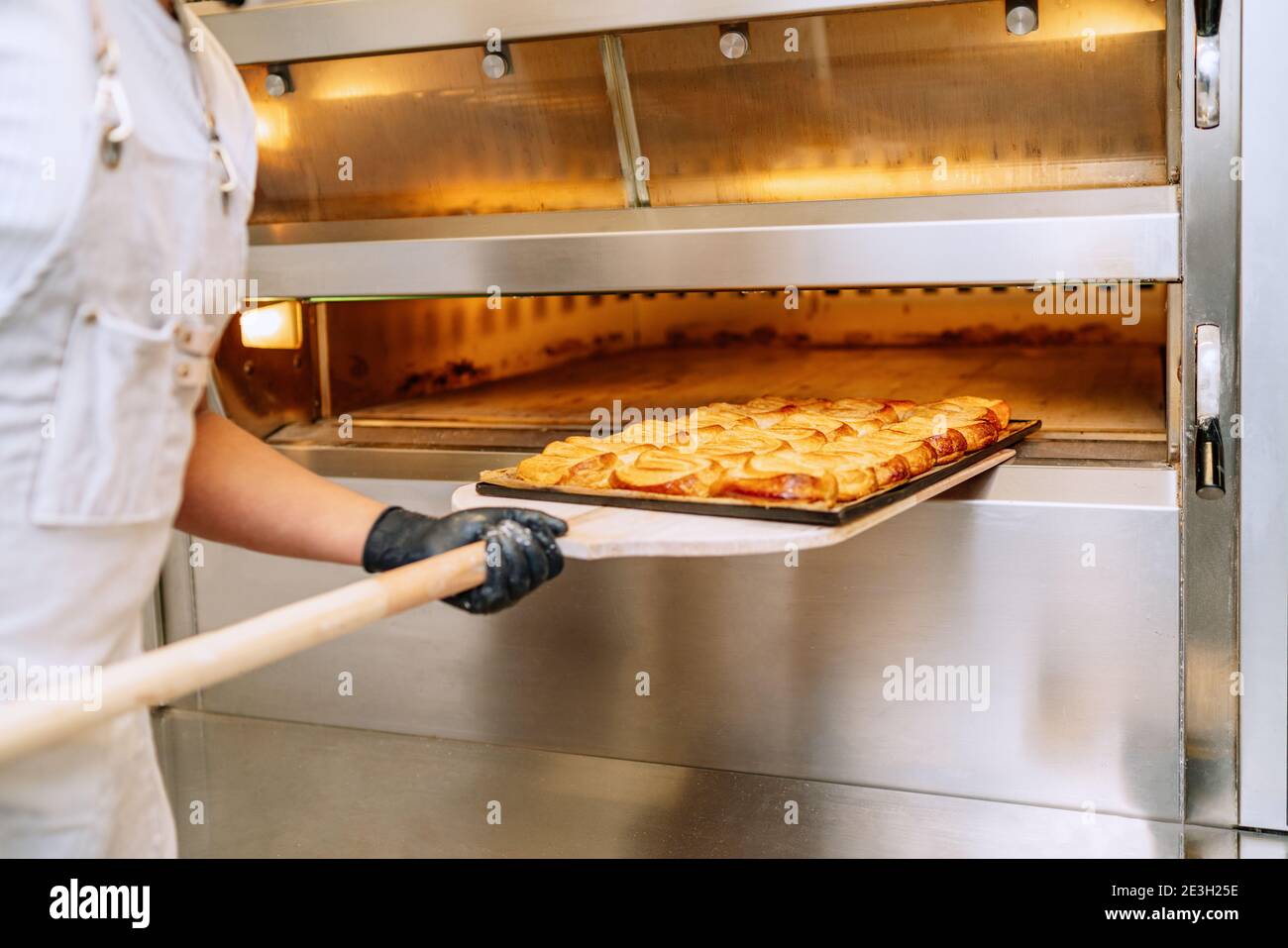 El panadero lleva una bandeja de palmas de pastelería en su las manos y lo  está poniendo en el horno de la panadería Fotografía de stock - Alamy