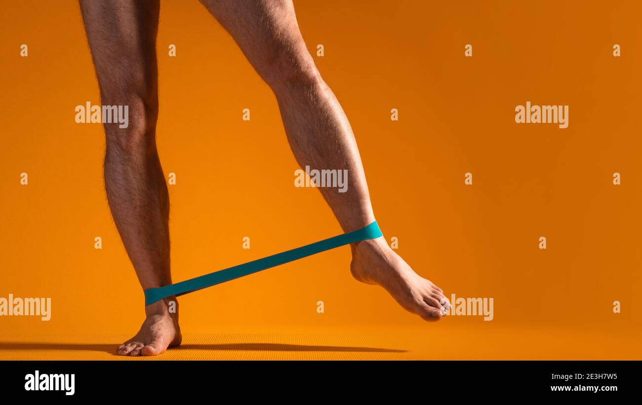 Musculosos piernas de los hombres con banda elástica para la aptitud, hacer ejercicios  para tensar los músculos de las piernas. Partes del cuerpo, fondo amarillo.  Copiar espacio a la derecha Fotografía de