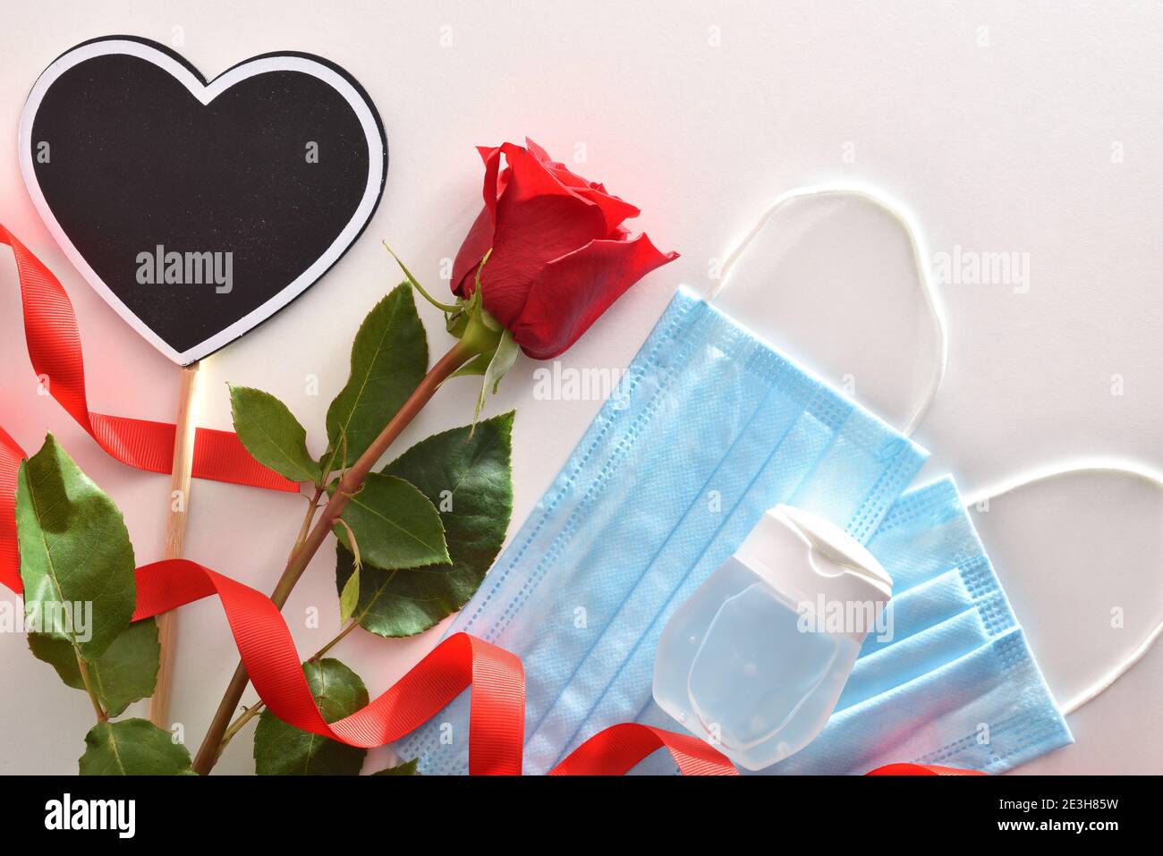 Fondo conceptual de la celebración del día de San Valentín con cartel con  texto feliz día de San Valentín y rosa con máscaras y gel hidroalcohólico.  Vista superior Fotografía de stock -