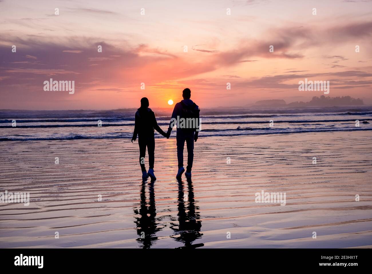 Pareja de hombres y mujeres de mediana edad viendo la puesta de sol en la playa de Tofino Vancouver Island Canadá, hermosa puesta de sol en la playa con colores rosa-púrpura en el cielo. Canadá Tofino Foto de stock