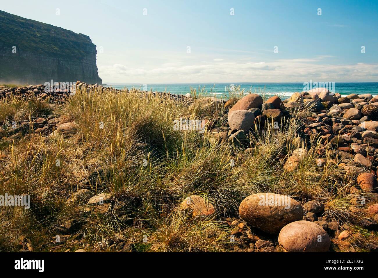 Piedras redondas grandes y hierba seca en la playa con Acantilado y mar en el fondo en la isla de Orkney ¡Ay! En verano Foto de stock