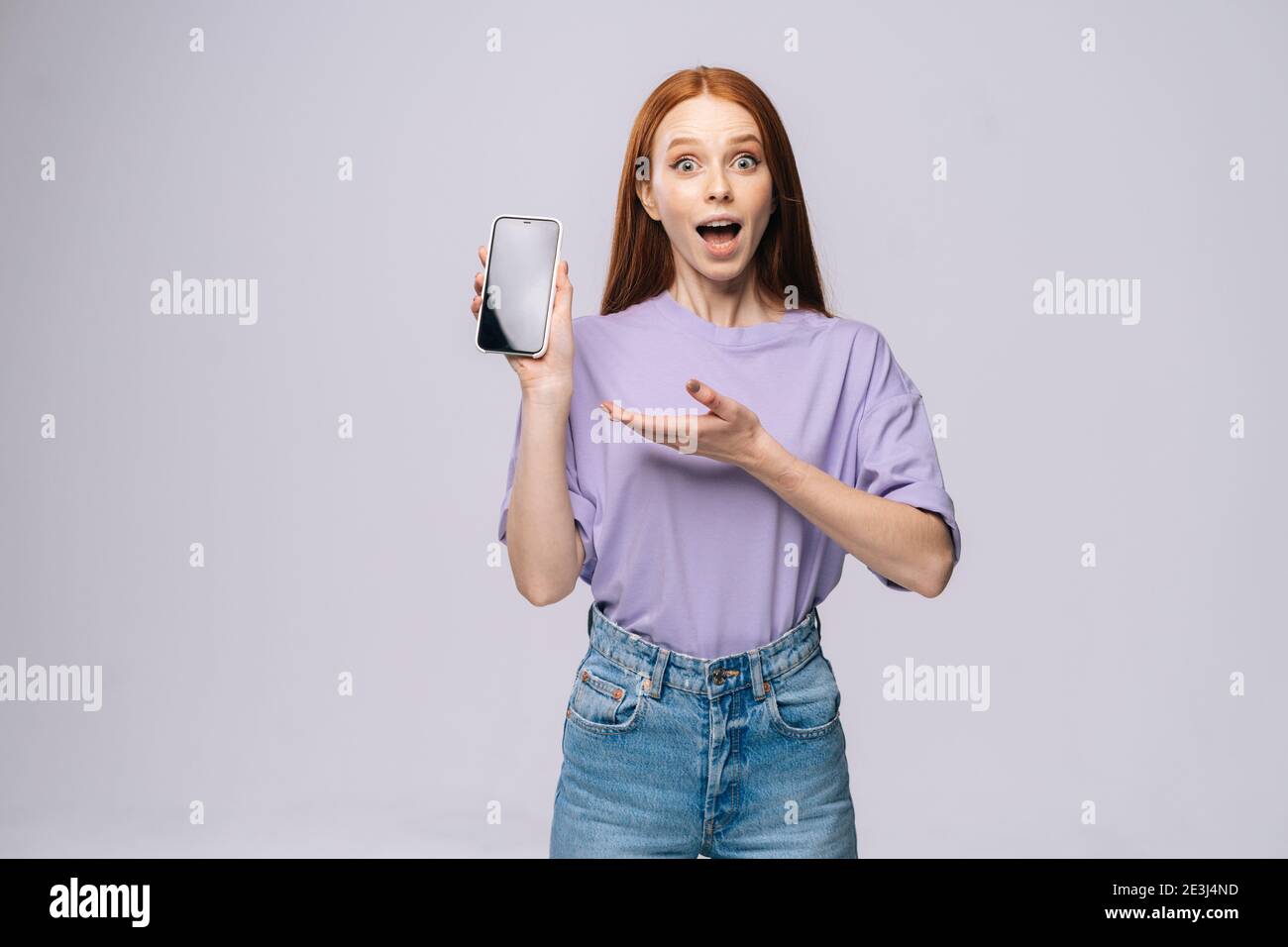 Feliz mujer joven conmocionada con ropa elegante informal apuntando con  palm en pantalla móvil en blanco Fotografía de stock - Alamy