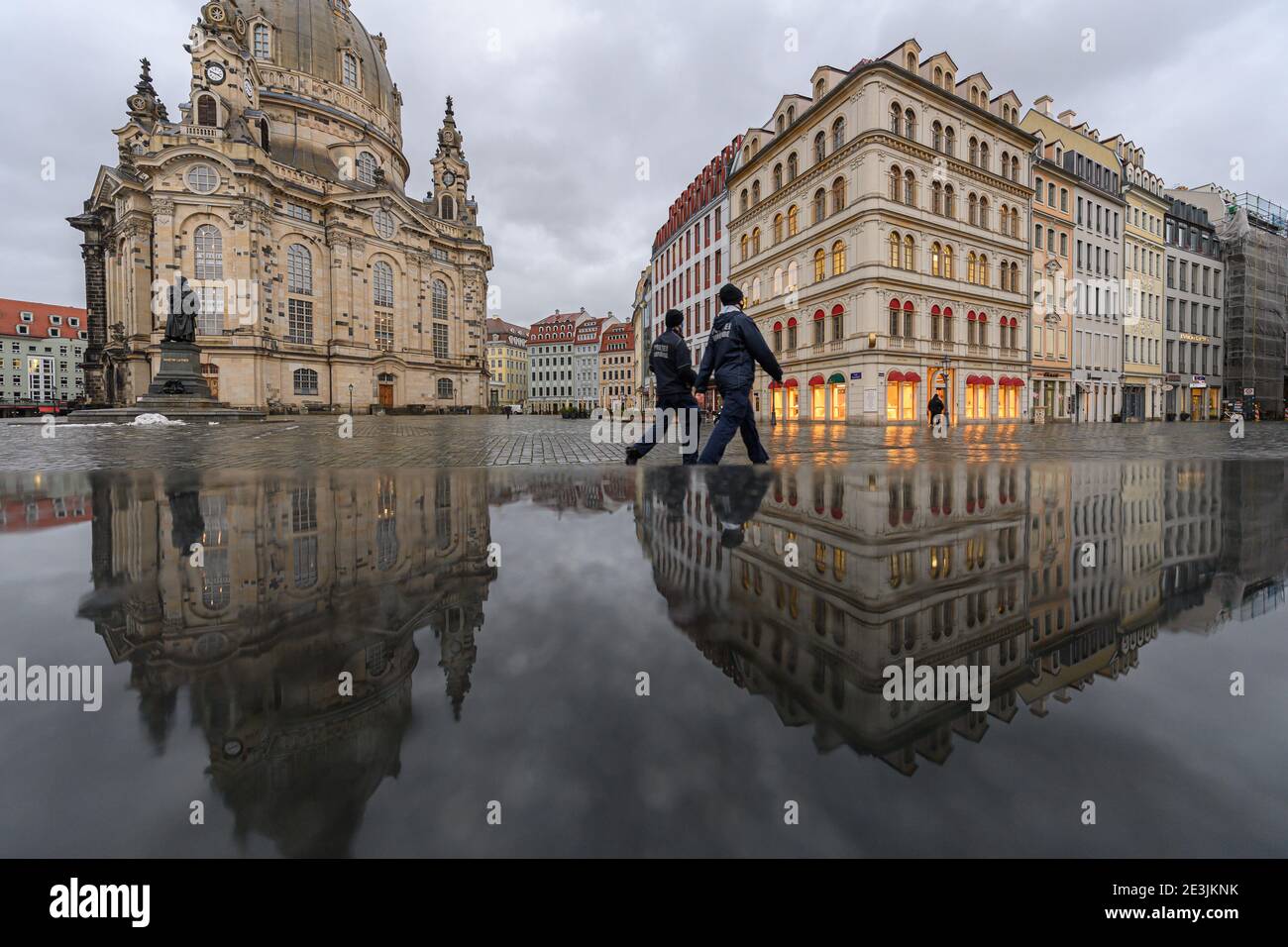 Dresde, Alemania. 19 de enero de 2021. La Frauenkirche y las casas de la Neumarkt se reflejan en un banco de piedra húmeda por la tarde, mientras que dos empleados del departamento de policía (Ordnungsamt) caminan a lo largo. Crédito: Robert Michael/dpa-Zentralbild/dpa/Alamy Live News Foto de stock