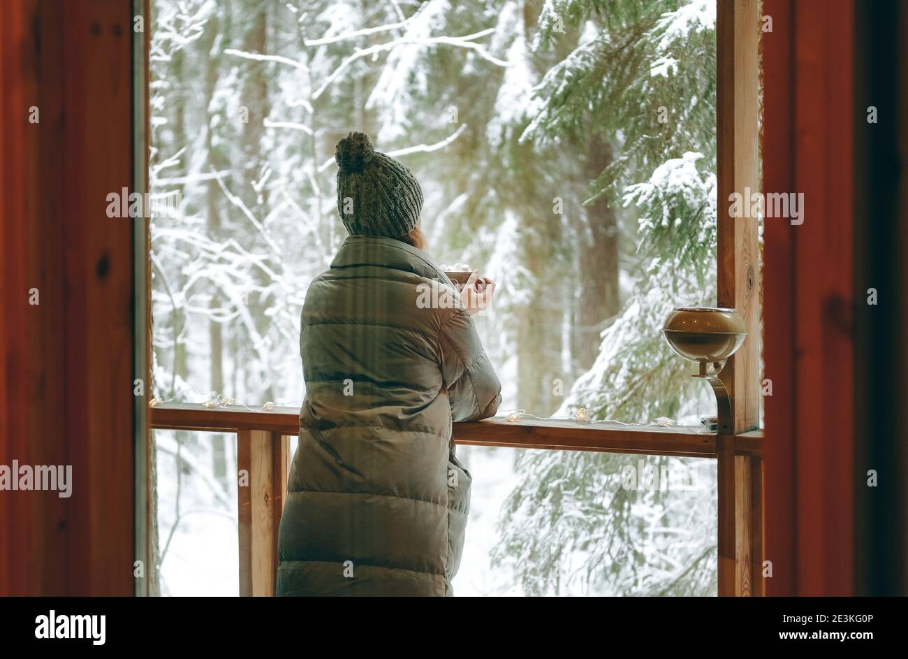 Mujer en invierno clother beber café en el balcón de la casa de campo en el paisaje de invierno. Foto de stock