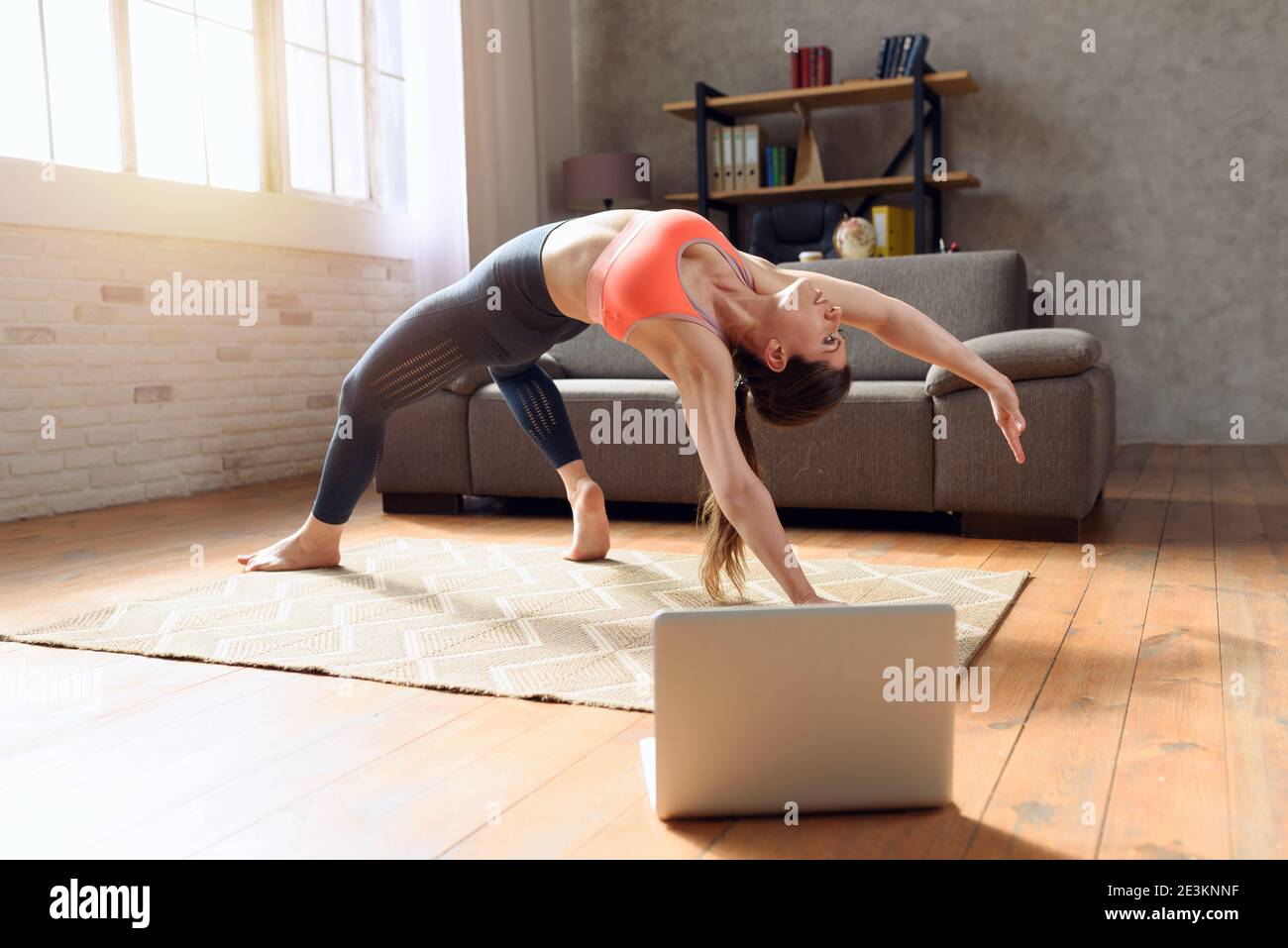 Una mujer joven sigue con un ordenador portátil un ejercicio de gimnasio. Está en casa debido a la cuarentena del coronavirus codigo-19 Foto de stock