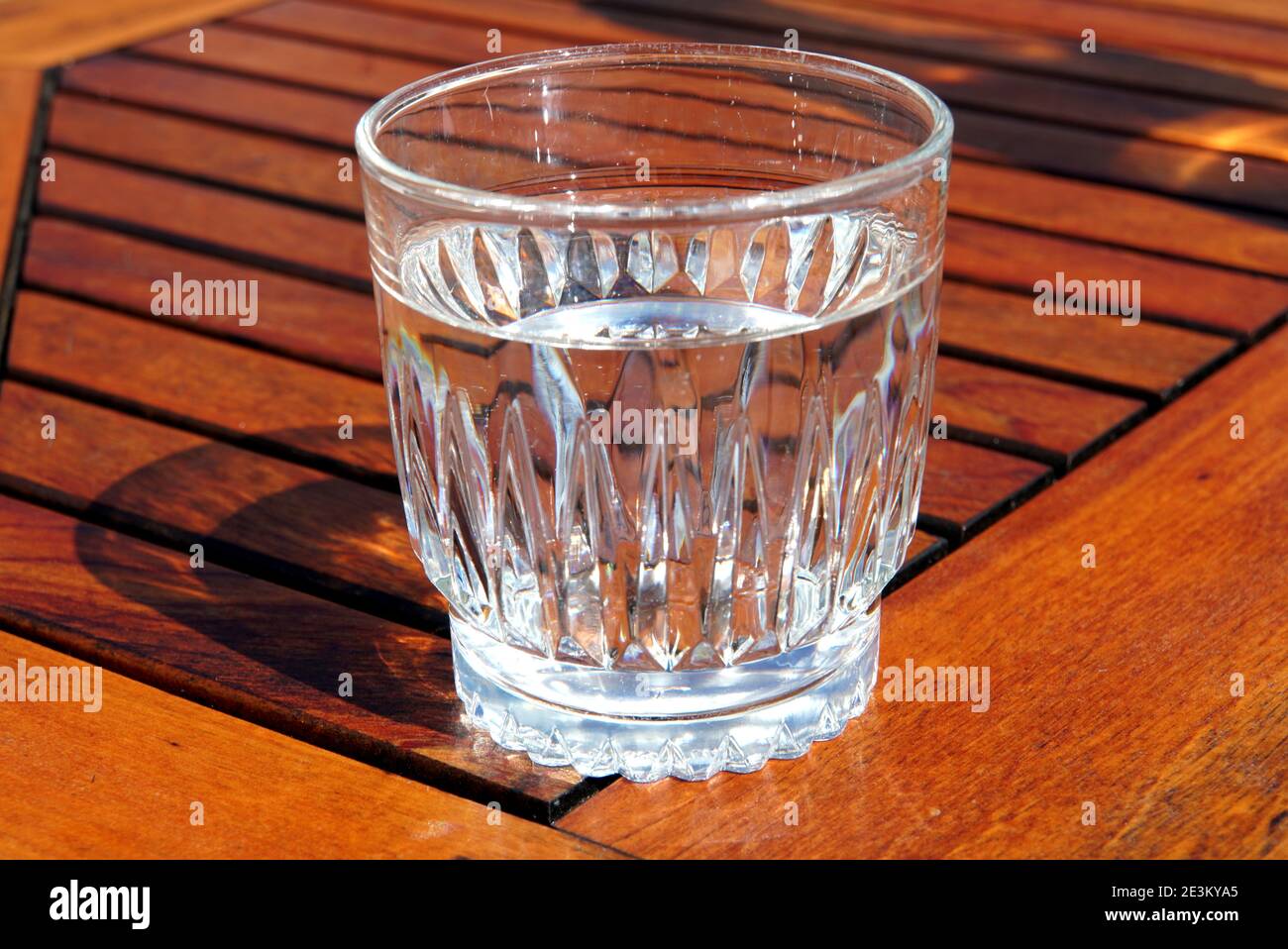 Un cristal transparente lleno de agua en la parte superior de una mesa de madera Foto de stock