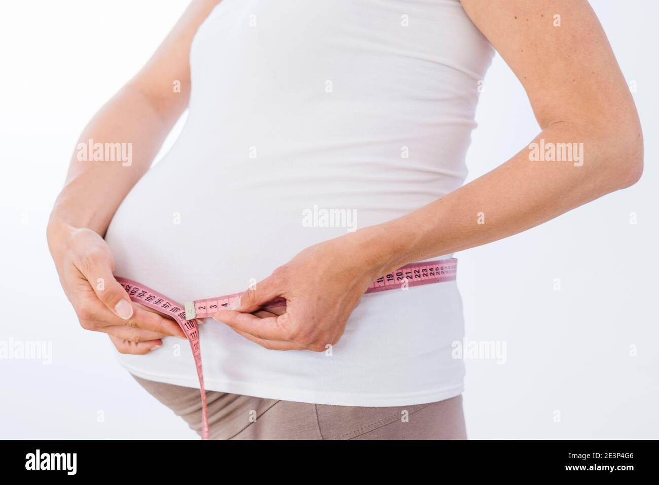 Mujer embarazada que mide su vientre grande sobre fondo blanco Foto de stock