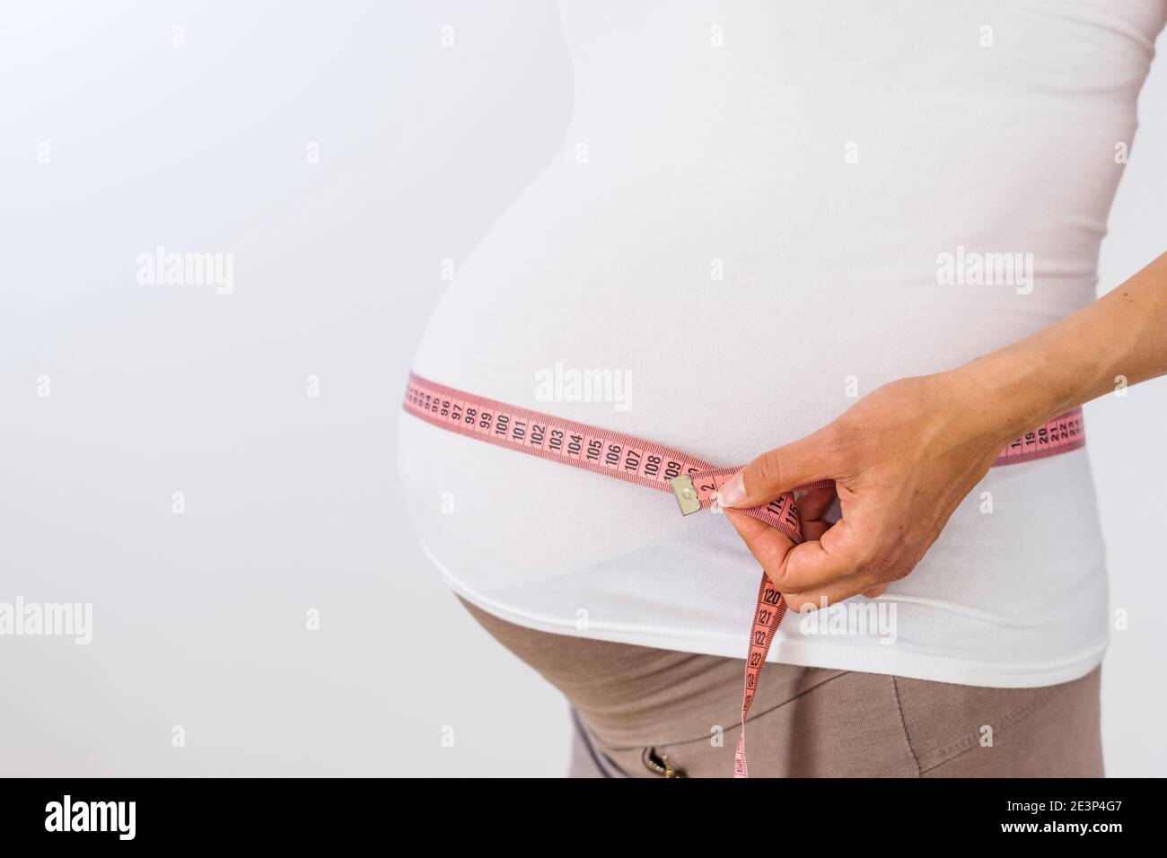 Mujer embarazada que mide su vientre grande sobre fondo blanco Foto de stock