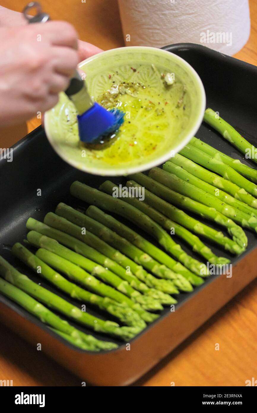 Cocine las grasas de espárragos verdes con aceite de oliva usando un azul  cepillo de cocción de silicona Fotografía de stock - Alamy