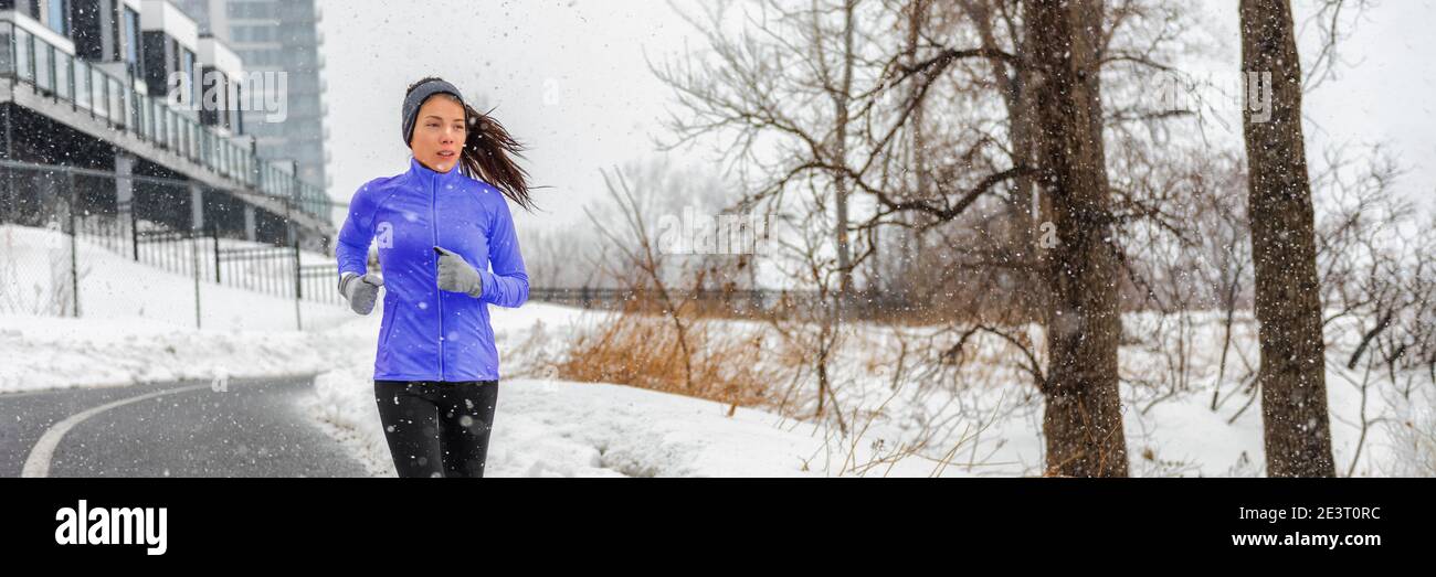 Invierno running chica asiática con chaqueta de invierno entrenamiento cardio fuera en copos de nieve caída durante el día frío al aire libre en la calle de la ciudad. Aptitud Foto de stock